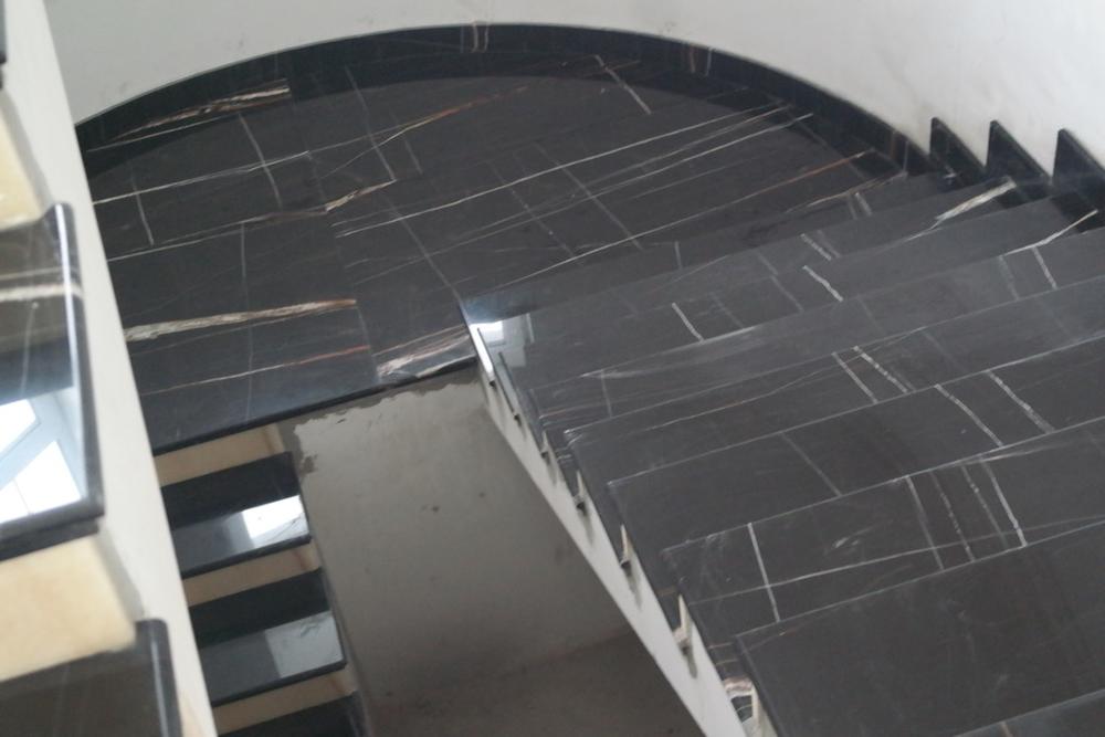 Лестница из мрамора Noir Saint Laureant выполнена по сложному проекту, подступенки из оникса Arco Iris