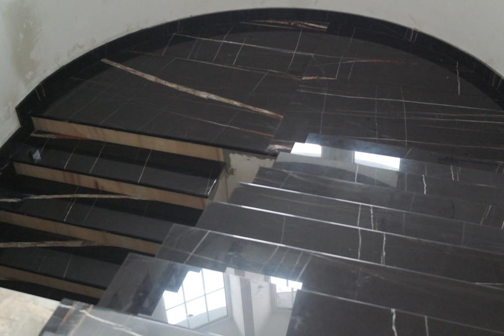 Лестница из мрамора Noir Saint Laureant выполнена по сложному проекту, подступенки из оникса Arco Iris